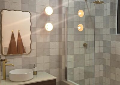 Modern bathroom design featuring a floating wood vanity, circular basin, brass fittings, and a walk-in shower with glazed tile walls.