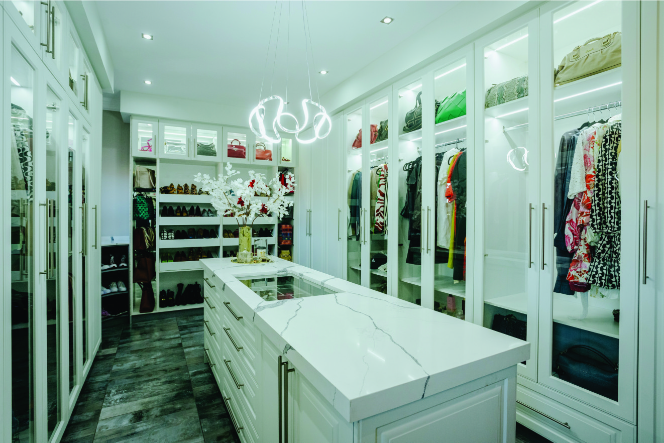Luxury walk-in wardrobe with glass-fronted cabinets, white shaker doors, marble island countertop, and LED lighting