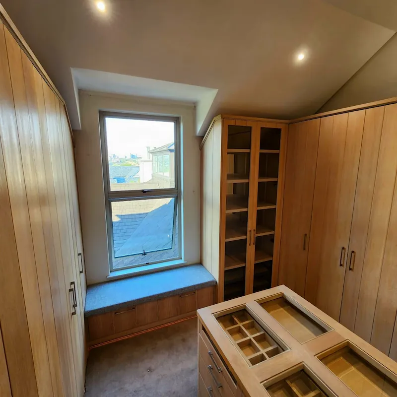 A classic and elegant walk in closet with natural timber elements complimented by glass detail cabinets and mirror backings.