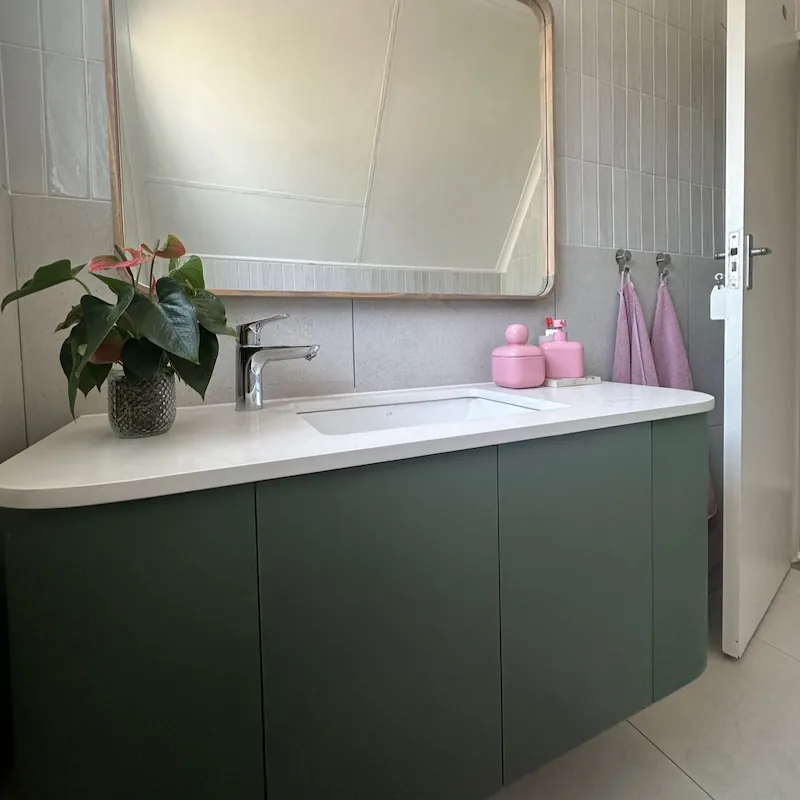 A custom bathroom vanity with sage green doors and rounded corners finished with a muted white counter top and inset sink