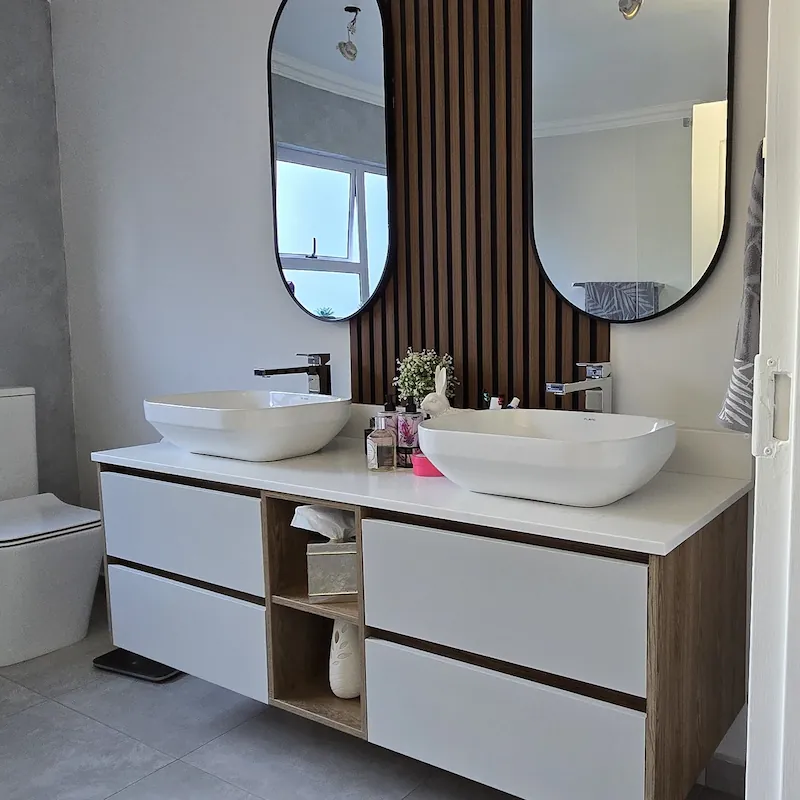 A luxury modern bathroom vanity with muted white counter top, sit on sink detail finished with light grey drawer detail and timber elements