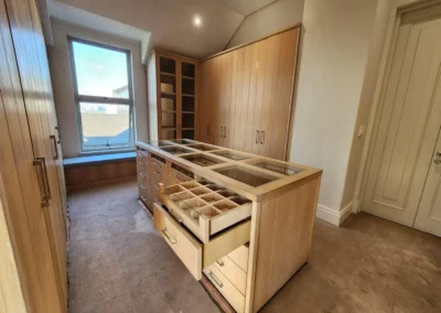 Custom walk-in closet at Waterfall Equestrian Estate with timber cabinetry, island drawer storage and glass display sections by Oakmont Kitchens & Interiors