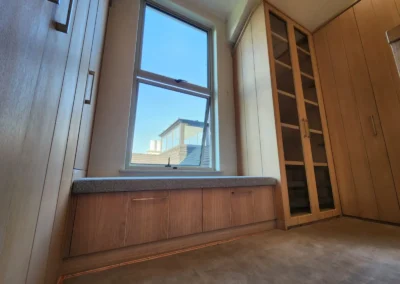 Custom walk-in closet with built-in window bench storage, timber wardrobes and glass-fronted display cabinetry at Waterfall Equestrian Estate