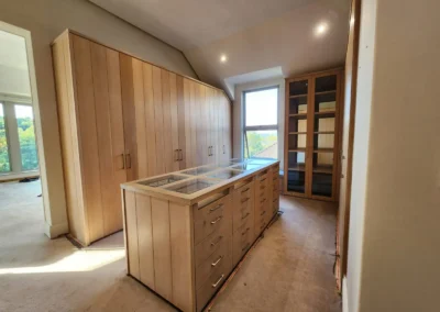 Walk-in closet in Waterfall Equestrian Estate with timber wardrobes, central drawer island, glass display tops and natural light