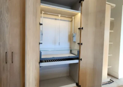 Walk-in closet interior with open wardrobe doors, hanging rails, shelves, pull-out trays and integrated lighting