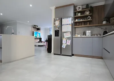 Open-plan custom kitchen cabinetry in Modderfontein with grey cupboards, timber shelving, integrated fridge and island storage