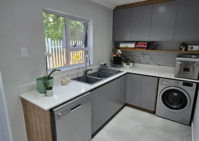 Custom kitchen utility area in Modderfontein with grey cabinetry, timber accents, sink, dishwasher, washing machine and practical storage